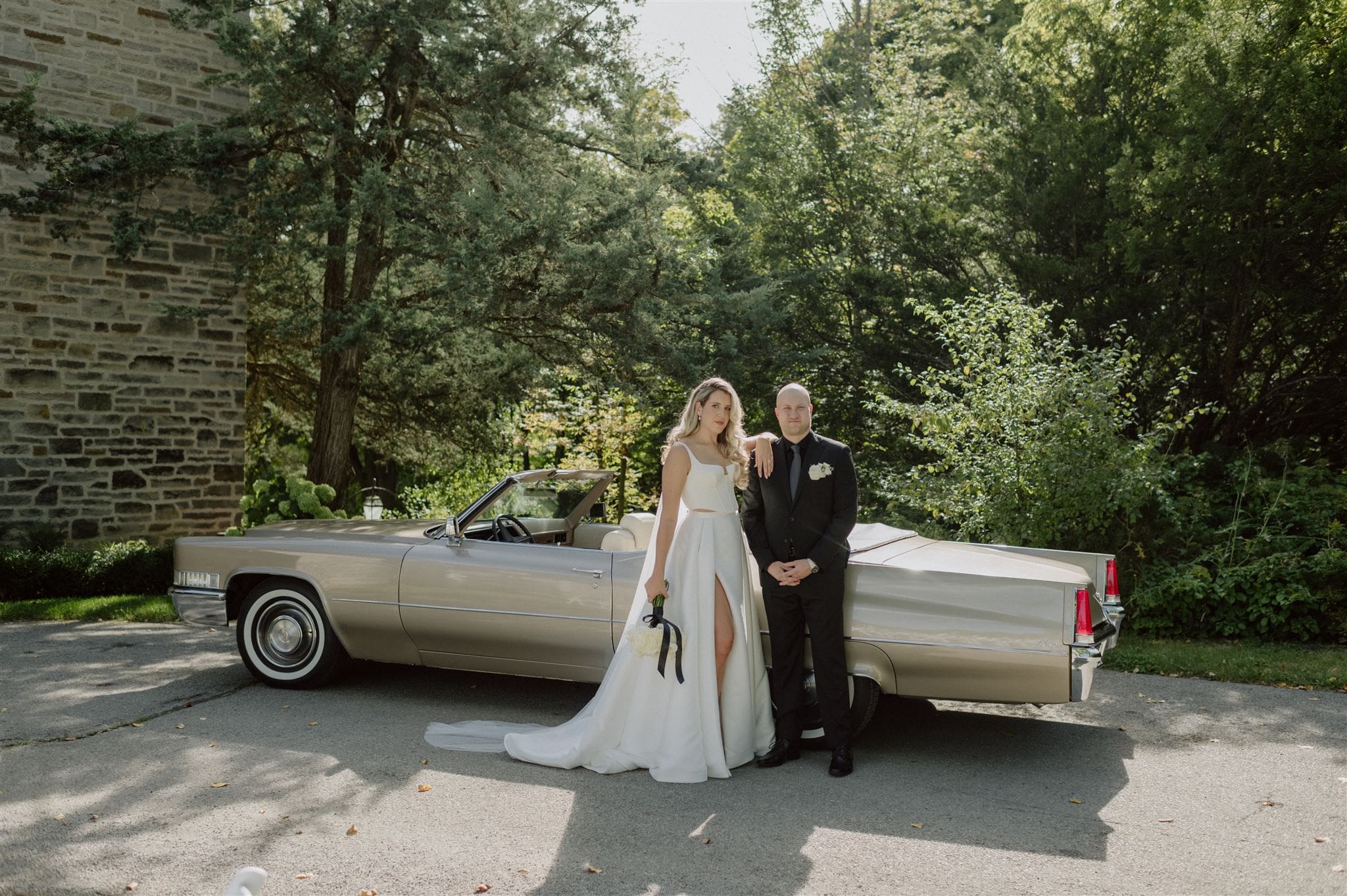 A bride and groom pose with a classic car in front of Eaton Hall wedding venue.